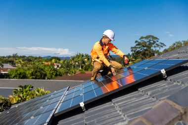 Solar panel technician with drill installing solar panels on house roof on a sunny day.